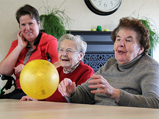 Twee bewoners en een medewerker lachen hartelijk tijdens een balspel activiteit