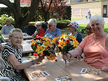 Senioren spelen gezellig samen bingo aan een buitentafel met kleurrijke bloemen