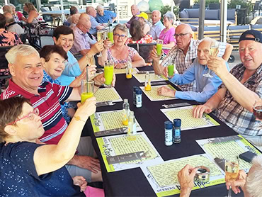 Diverse groep mensen heft vrolijk hun drankjes tijdens een gezellig samenzijn in De Klaproos