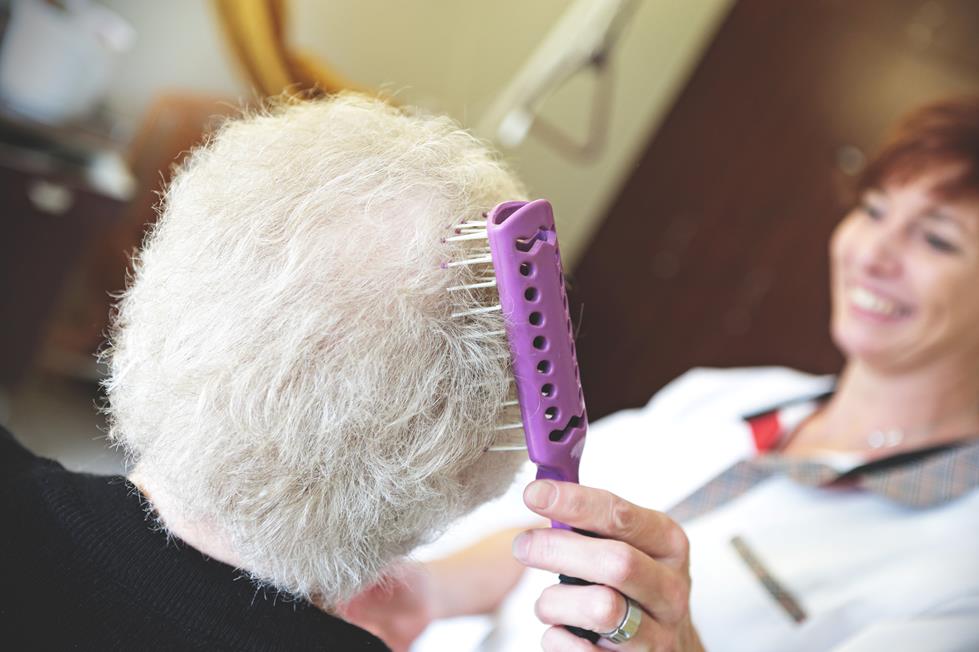 Kapper borstelt het witte haar van een oudere dame met een paarse borstel